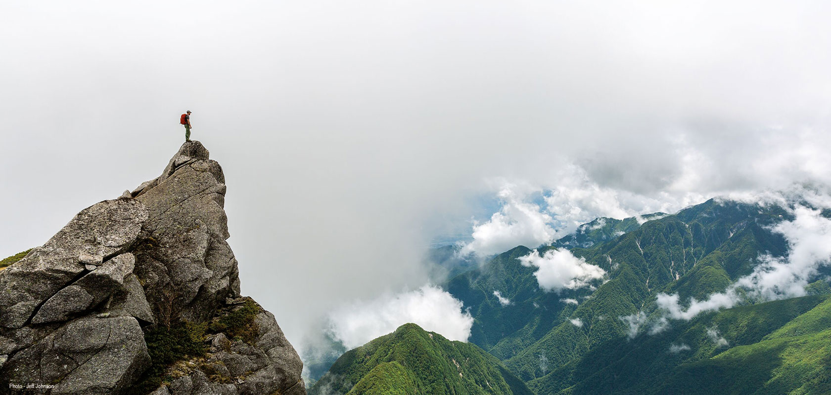 A person is standing on a rock and looking at the mountains, wearing Patagonia kit.