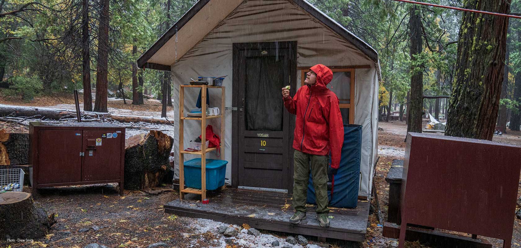 A person is standing under a hut roof, while it is raining, wearing Patagonia clothes.