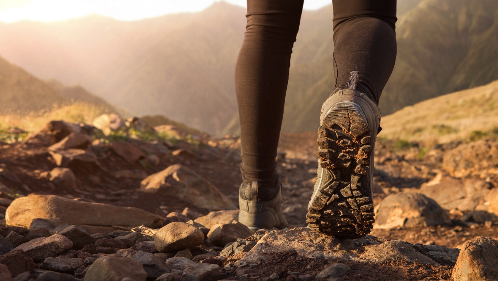 Close up of hiker boots trekking in the mountains at the sunrise with copy space
