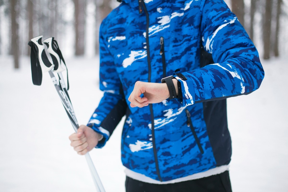 A man holding ski poles looking at his watch 