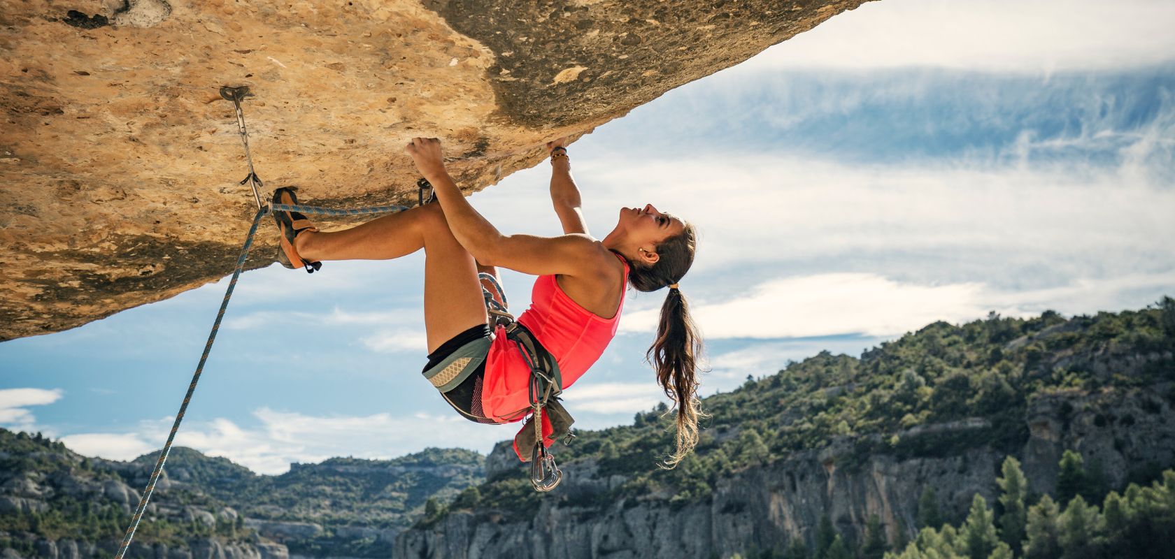An image of a woman climbing a rock face wearing a climbing harness