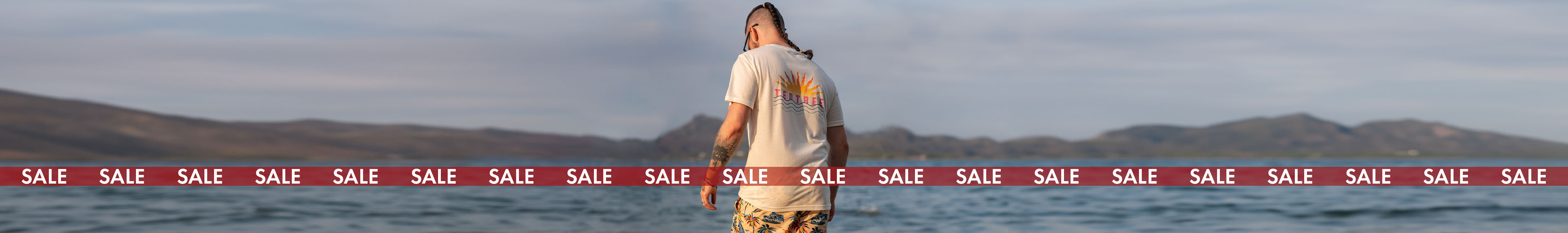 Men's sale. A man is by the sea, wearing t-shirt and shorts. 