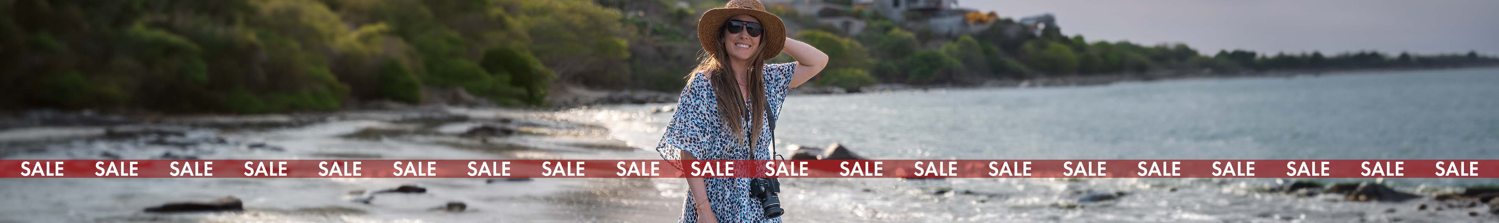 Women's sale. A woman is by the sea, wearing summer clothing, a summer hat, and sunglasses 