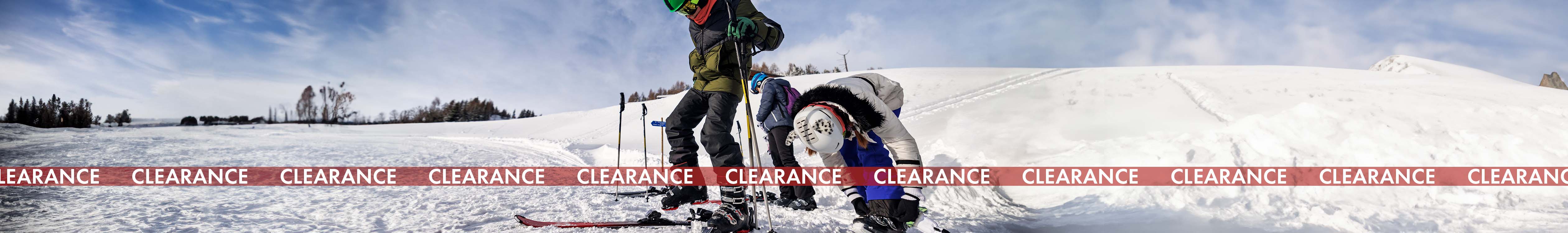 Shop snowsports equipment clearance. Two skiers adjusting snowsports equipment on the snow