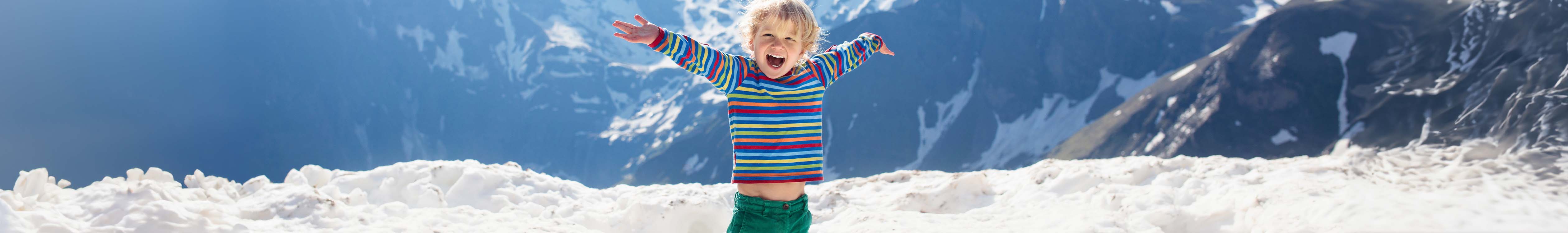 Shop Kid's baselayers. A kid standing outside in a stripey top with arms wide stretched