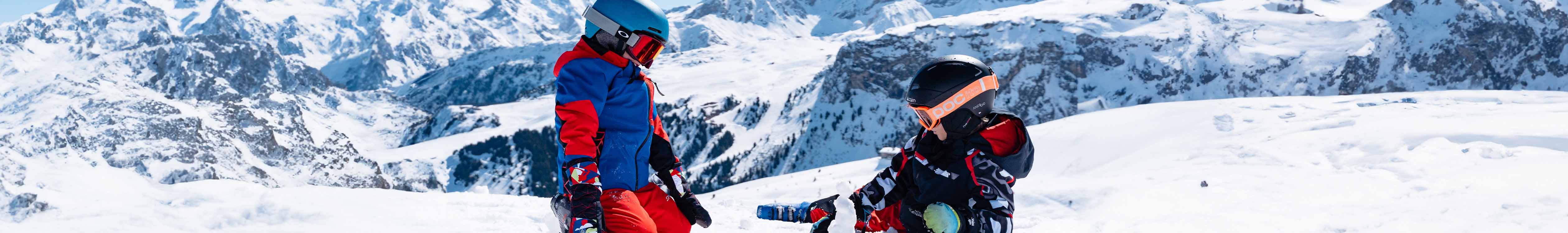 Shop Kid's helmets. Two children wearing helmets  and full ski kit standing outside in the snow
