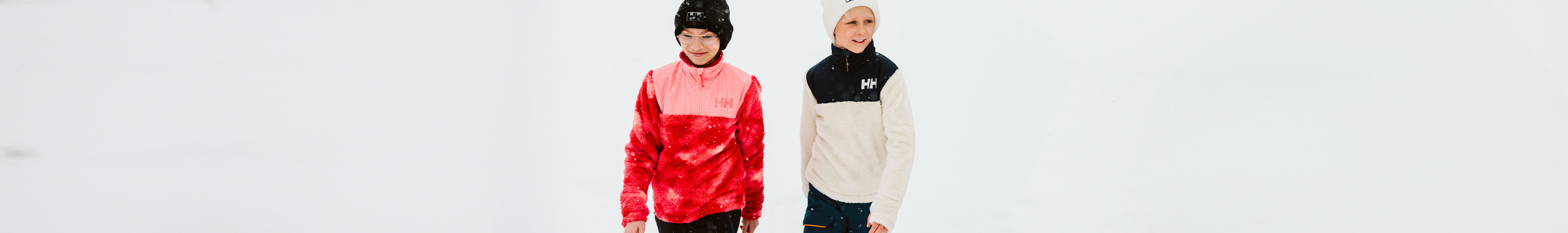 Shop kid's midlayers. Two kids standing outside wearing Helly Hansen fleeces
