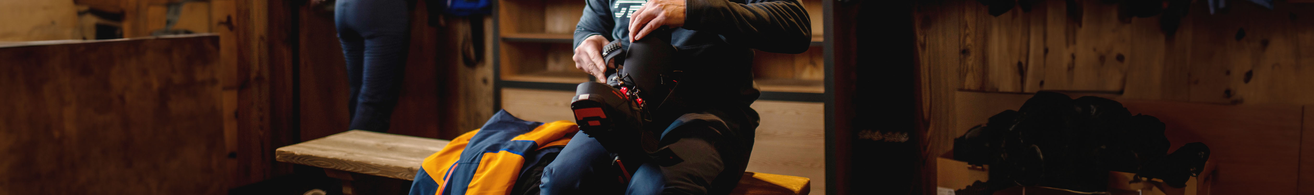 Shop men's footwear. A man in a boot room putting on snow boots. 