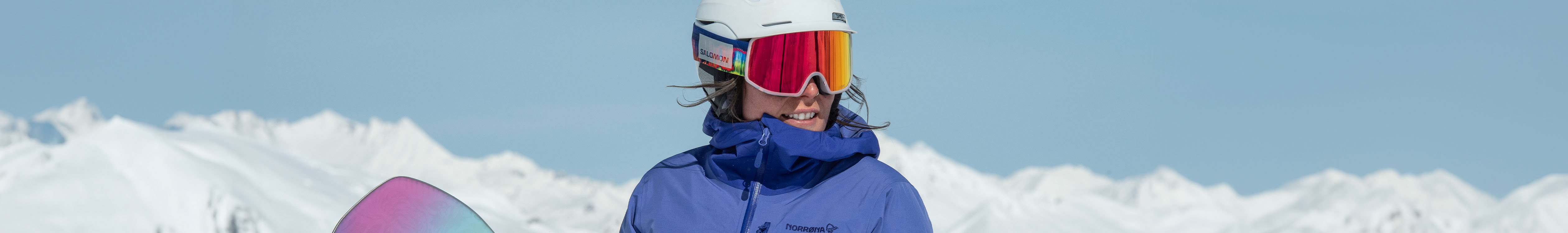 Shop goggles. A woman wearing orange ski goggles in front of a snowy backdrop 