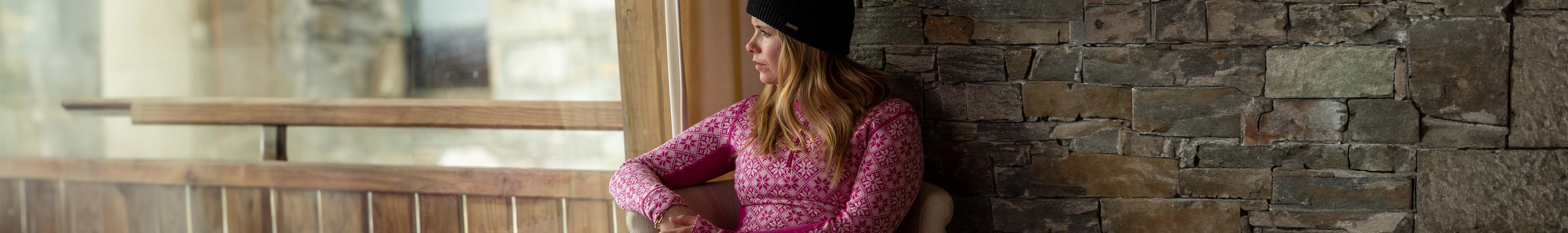 Shop Women's baselayers. A woman looking out a window in a chalet 