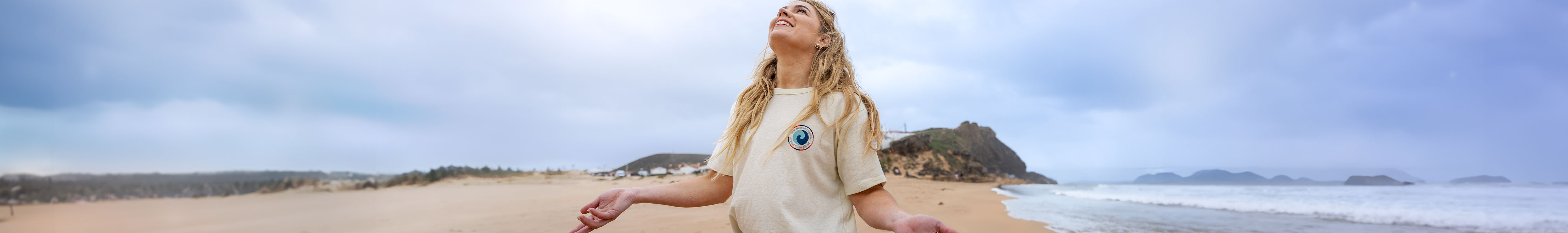 Women's summer styles. A woman is smiling and looking at the blue sky, wearing a white t-shirt on the beach