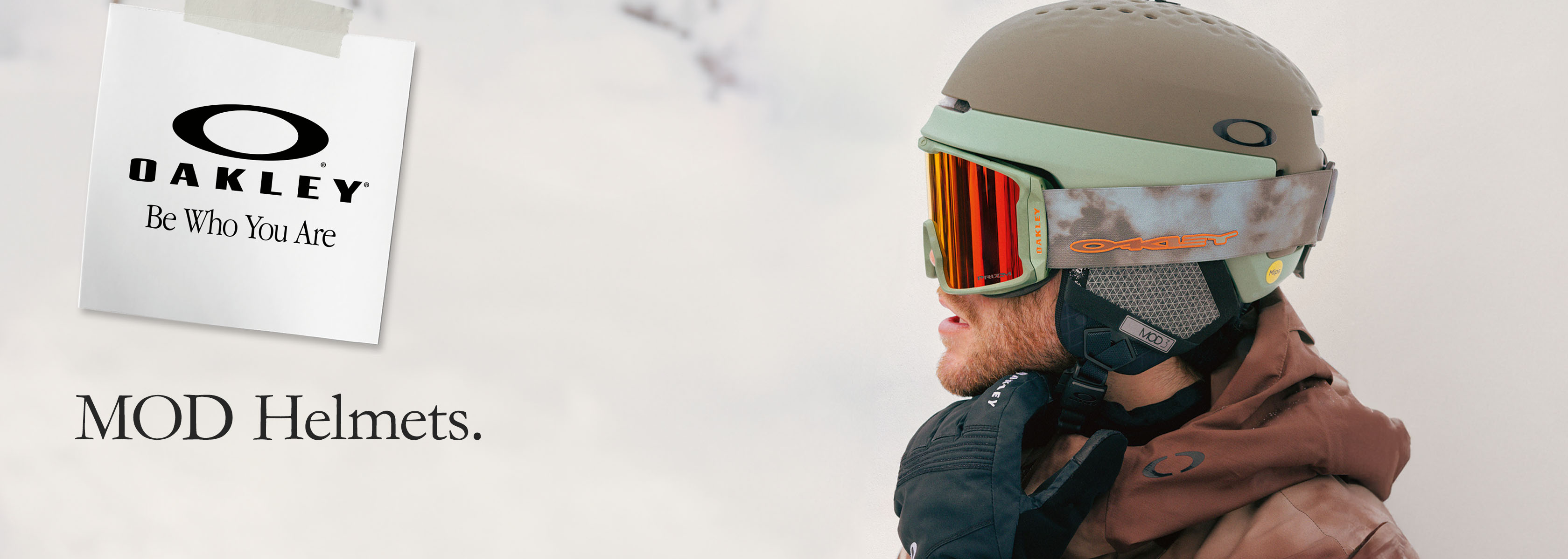 A man in an orange coat holds up the Oakley Mod 5 and Mod 1 helmets