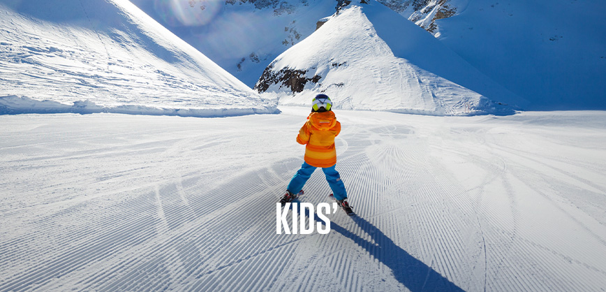 Shop kids new season. Kid in orange jacket and blue troursers skiing on the piste