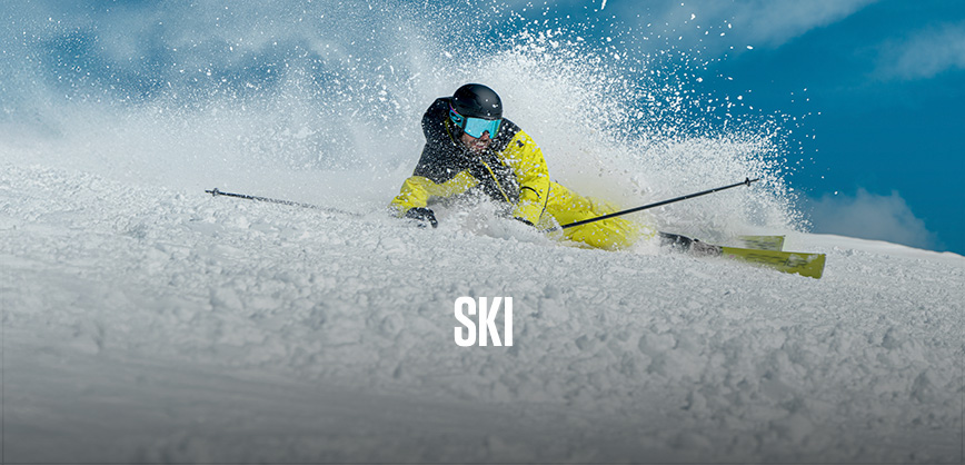 Shop ski new season. A person in yellow ski gear skiing down the mountain