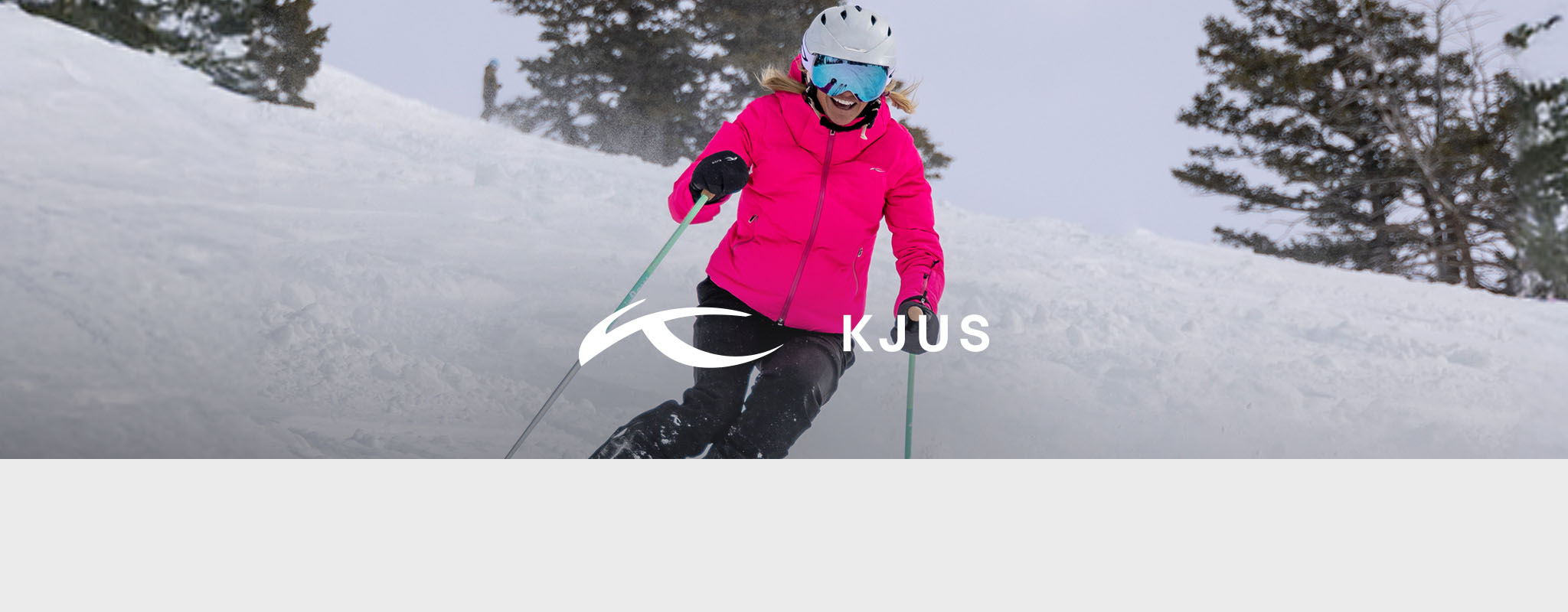 Shop Kjus collection. Women in bright pink jacket skiing down the mountain