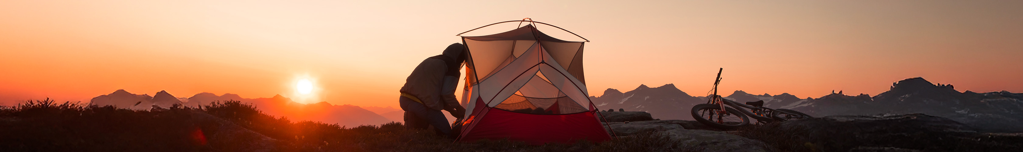 Shop light and versatile camping equipment. A person setting a small tent at sunset