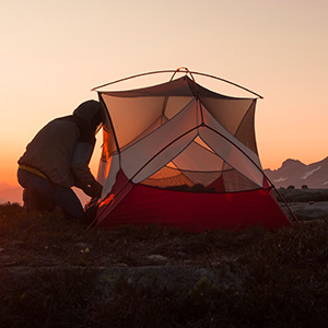 Shop light and versatile camping equipment. A person setting a small tent at sunset