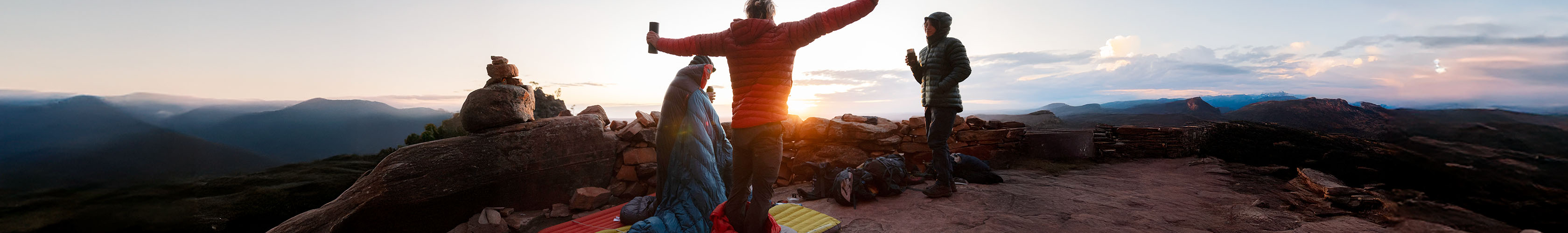 Shop sleepingbags, mats + liners. Three people waking up in their sleep bags on the mountain