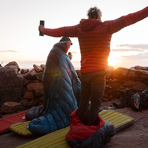Shop sleeping bags, mats + liners. Three people waking up in their sleep bags on the mountain