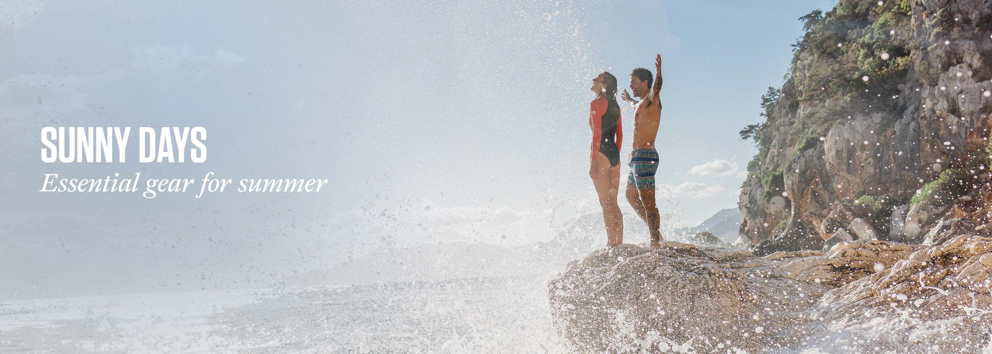 Shop Hot Weather essentials. A man and a woman standing on a rock by the sea