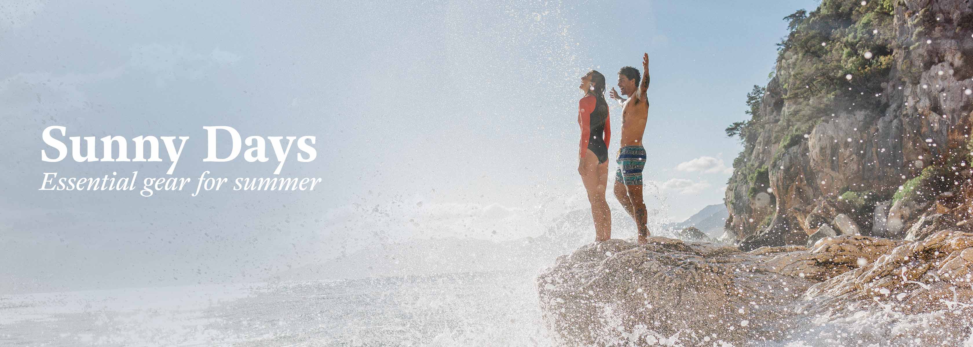 Shop Hot Weather essentials. A man and a woman standing on a rock by the sea