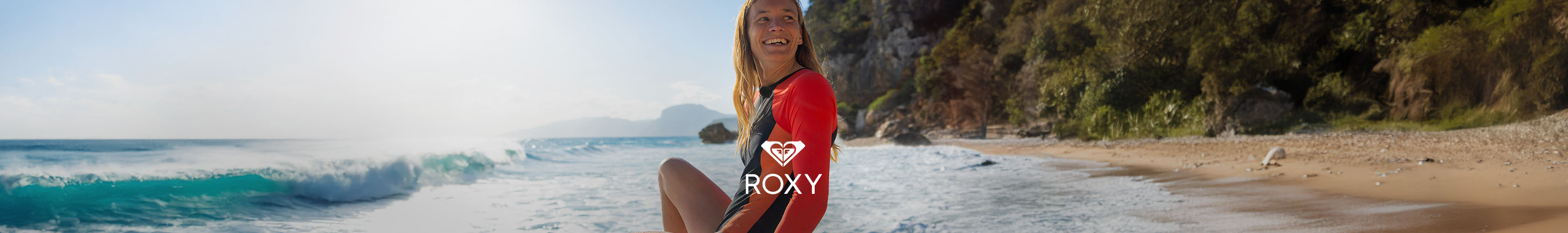 Shop Roxy clothing collection. A woman in surfer swimmsuit sitting on a beach
