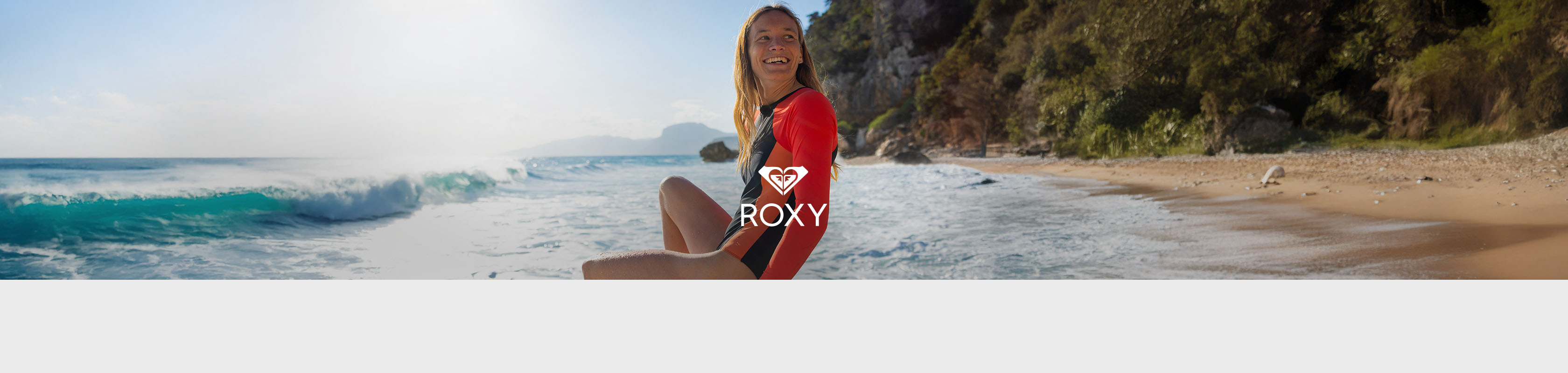 Shop Roxy clothing collection. A woman in surfer swimmsuit sitting on a beach