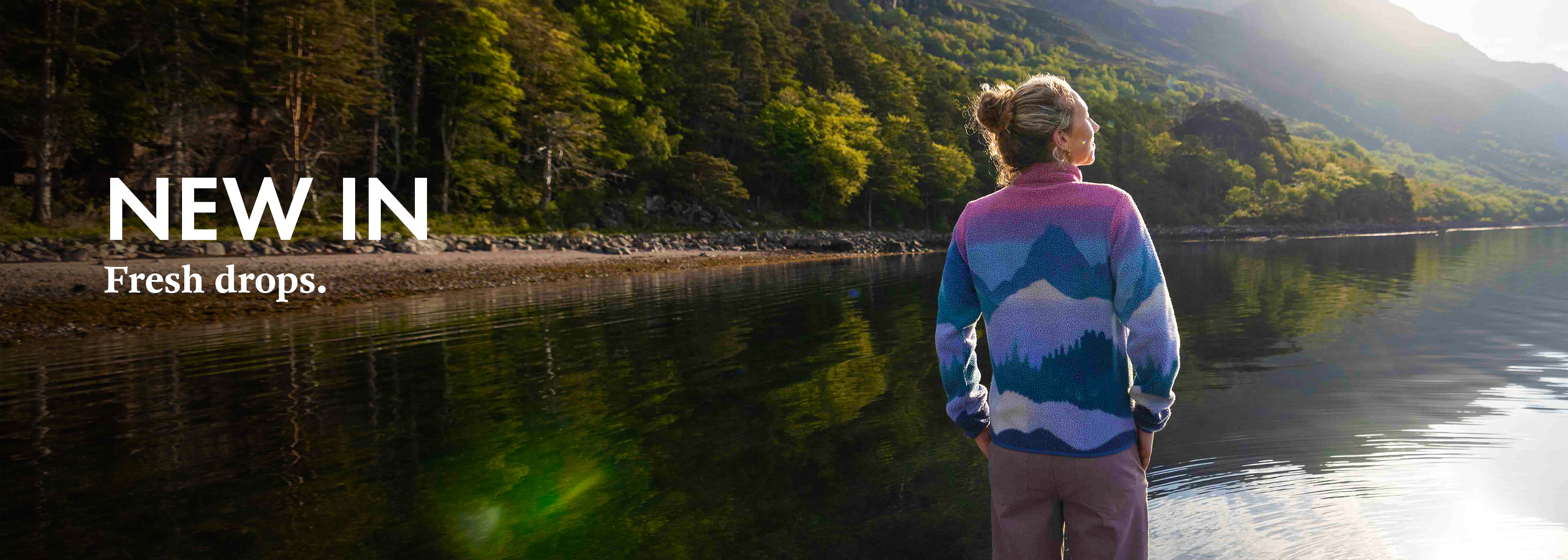 Shop new in. Woman in colorfull jumper is standing by a lake in a woods