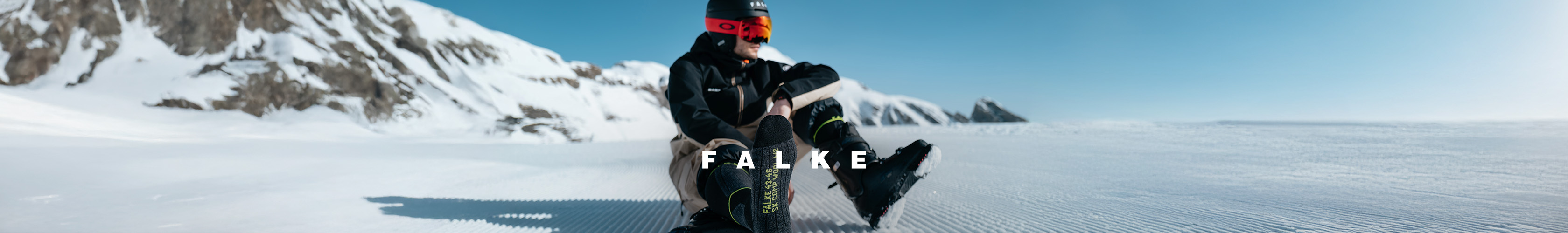Shop Falke socks. A skiier resting on a snowy slope in Falke socks