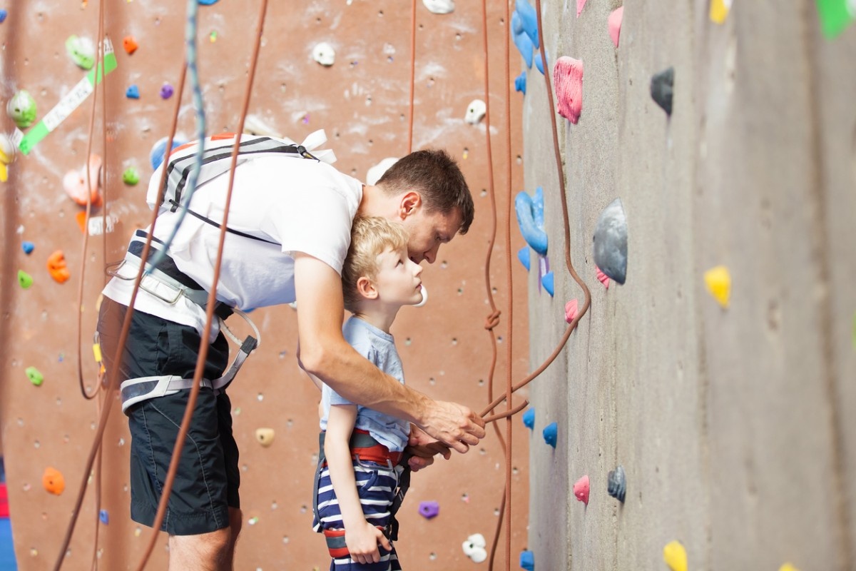 A father helping his son with his climbing harness and ropes