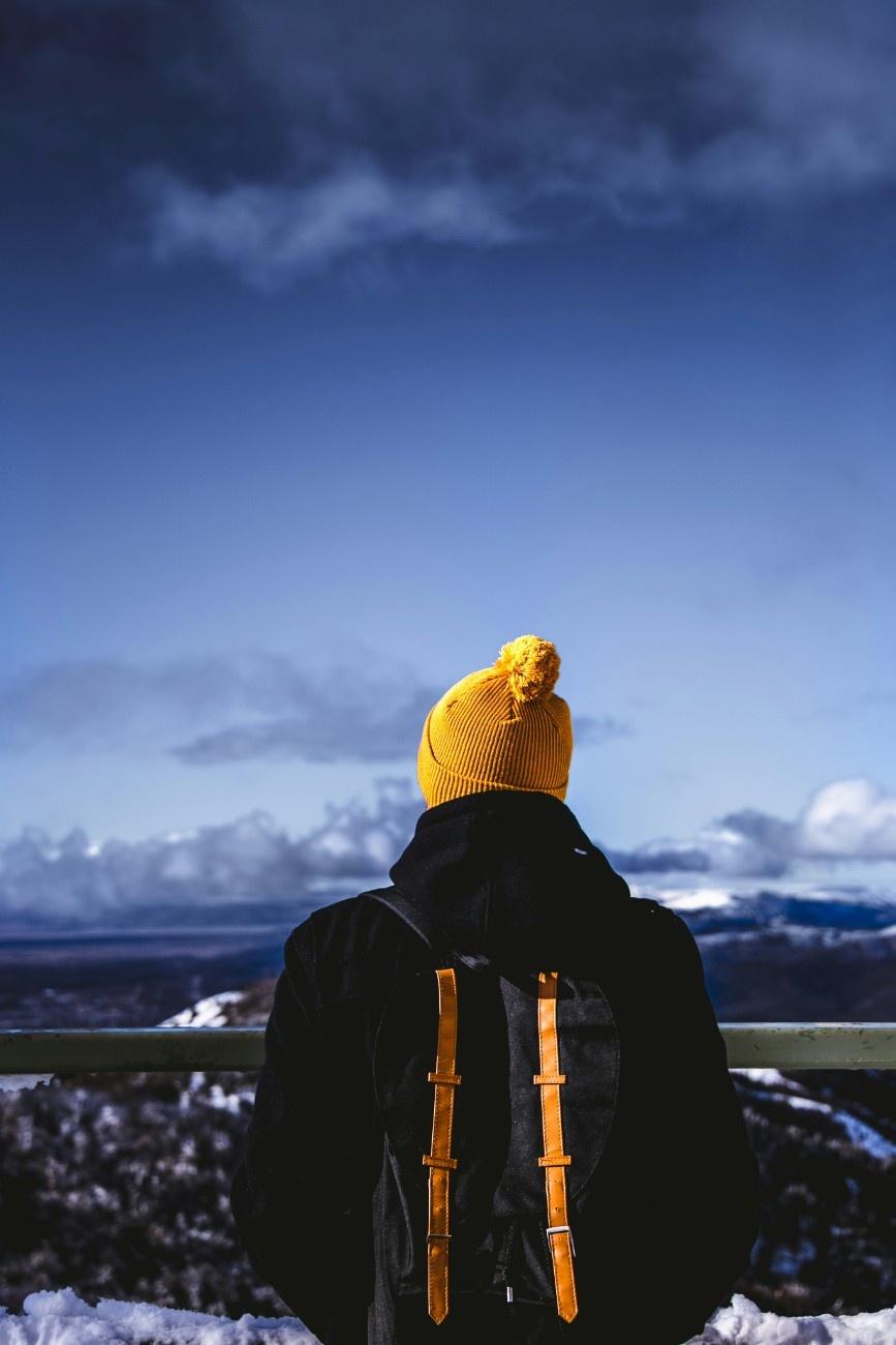 A man wearing a yellow beanie hat looking out at a winter landscape